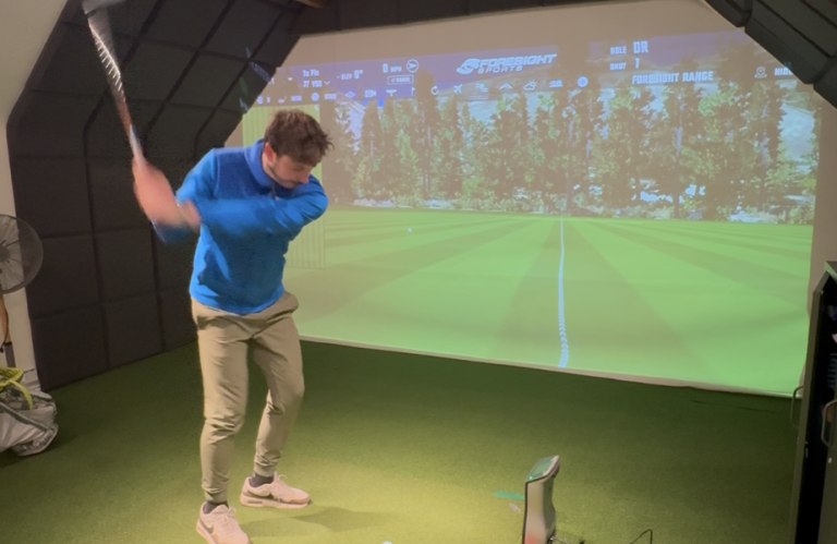 A golfer swings in a simulator with a virtual golf course displayed behind. Cheshire  West Golf Academy